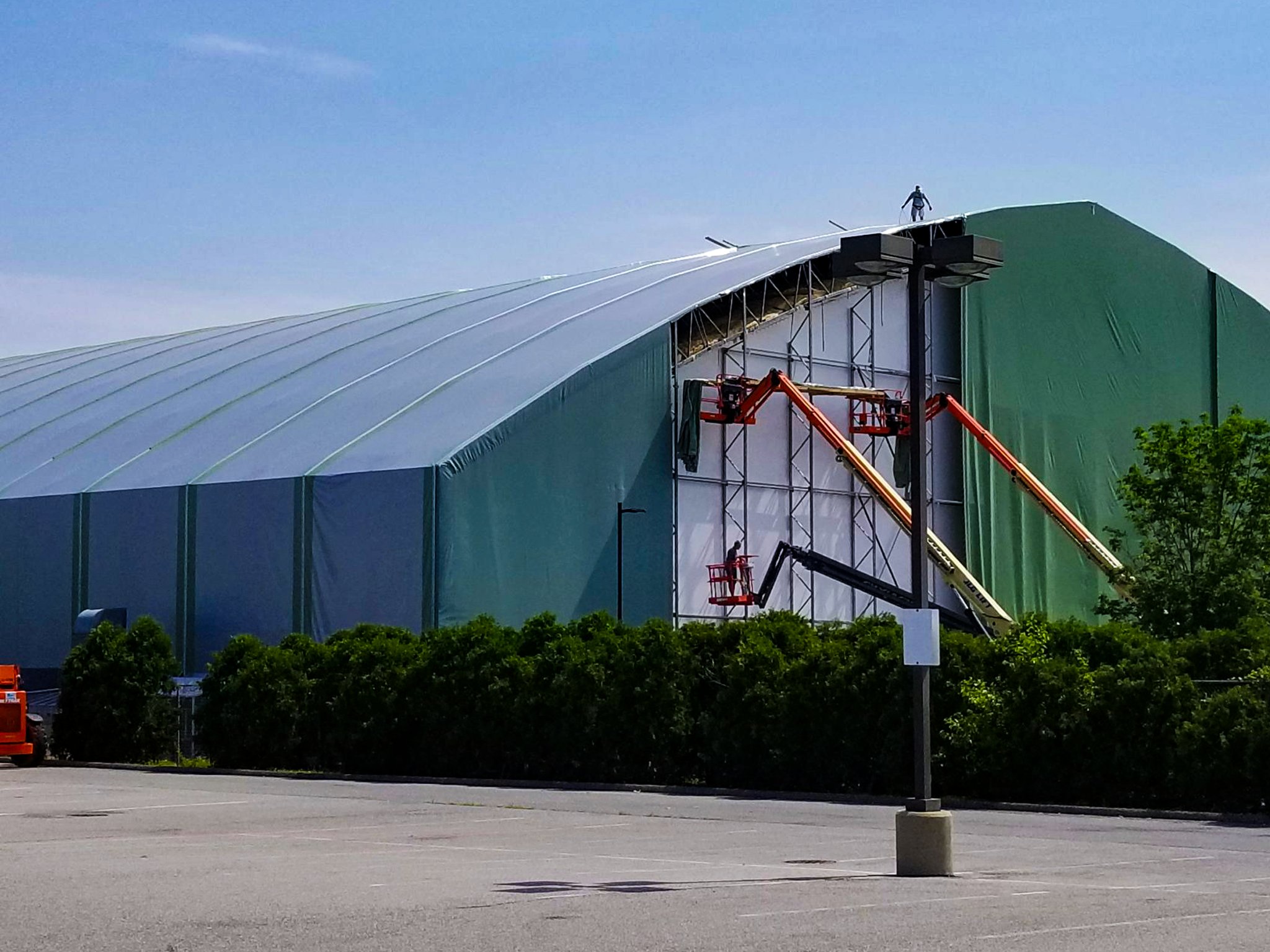 Crews on aerial lifts and scaffolding at the end wall of a large fabric-covered frame building