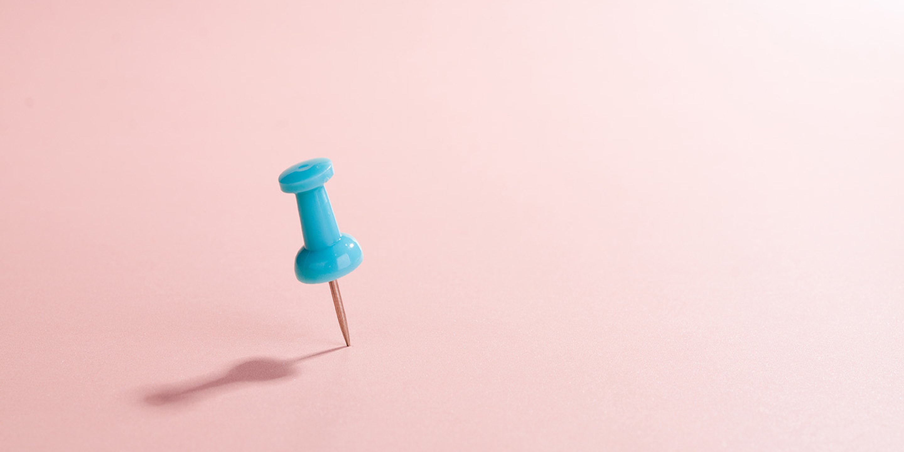a blue push pin on a pale pink background