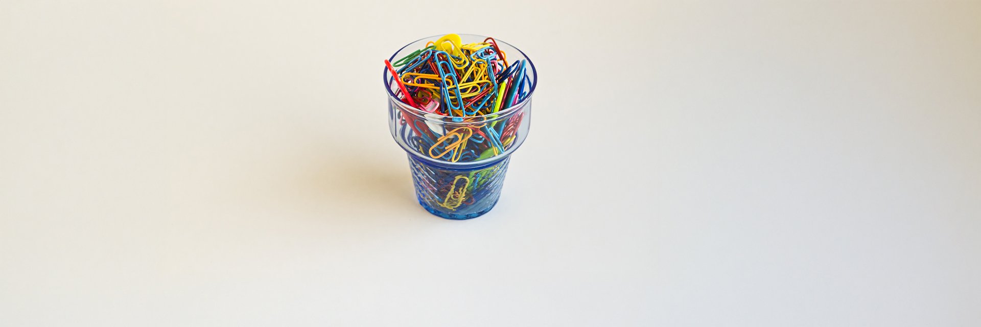 a cup of colorful paperclips on a white background