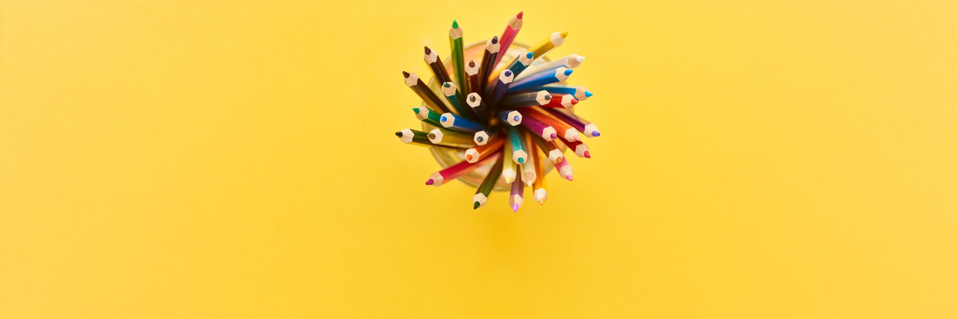 A top view of colored pencils in a cup on a yellow background