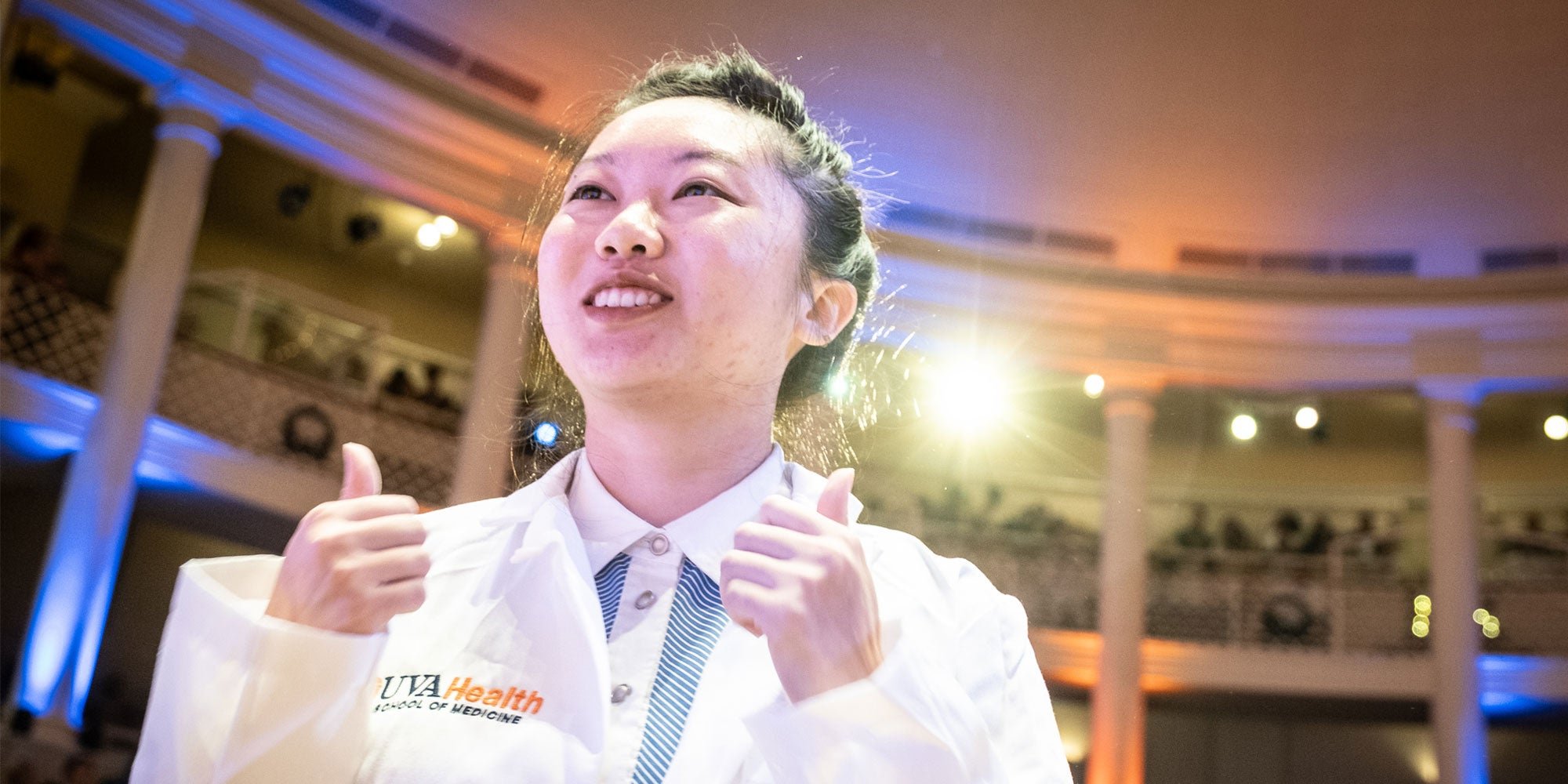 student in white coat with thumbs up